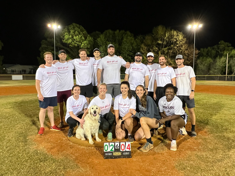 residents softball team with a dog posed at a pitcher's mound at night